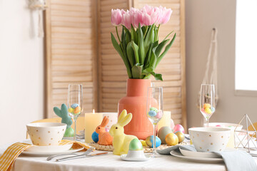 Beautiful table setting with candles, painted eggs and Easter bunnies in dining room