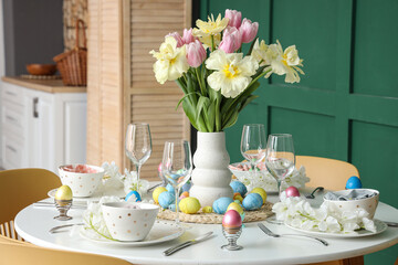 Stylish Easter table setting, painted eggs, glasses and vase of flowers in dining room