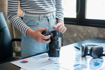 A photographer adjusts camera settings in a modern office, surrounded by charts and headphones on a desk.