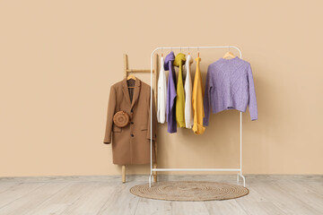 Rack of stylish clothes and rug near beige wall