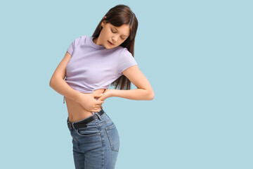 Young woman suffering from back pain on light blue background