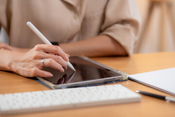 Closeup hand young businesswoman using tablet while writing on desk in living room at modern home office, business woman using tablet, entrepreneur or freelance, business and commercial.