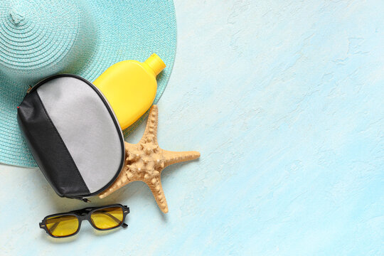 Cosmetic bag, hat, sunglasses, starfish and sunscreen on blue background