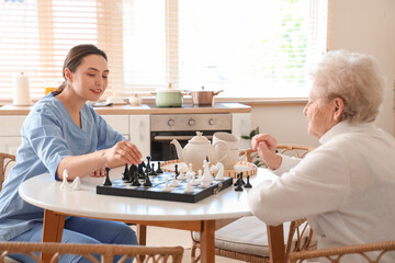 Physical therapist with senior woman playing chess at table in kitchen
