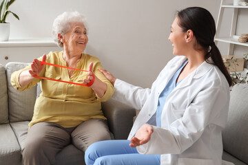 Obraz premium Senior woman with stretching band and physical therapist at home