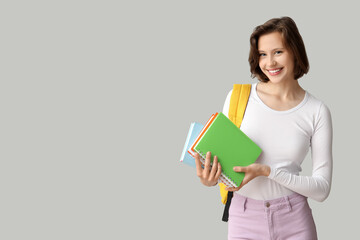 Happy female student with backpack and notebooks on grey background