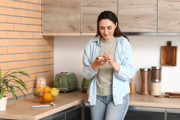 Diabetic young woman using glucometer in kitchen