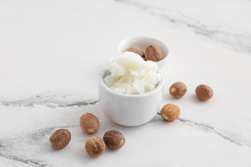 Bowls with shea butter and nuts on light marble background
