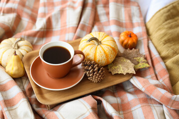Cup of coffee with fir cone, pumpkins and autumn leaves on bed, closeup