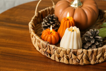 Wicker basket with burning candles in shape of pumpkins and forest bumps on coffee table at home, closeup