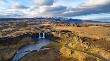Scenic icelandic landscape featuring waterfall, remote road, and distant snow mountains