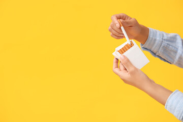 Female hands with pack of cigarettes on yellow background. Stop smoking concept