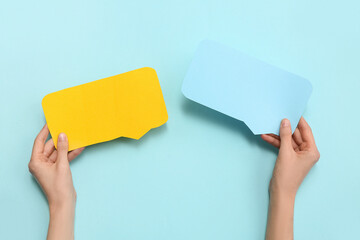 Female hands with blank paper speech bubbles on color background, closeup