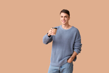Handsome young man in stylish blue sweater with paper cup of hot coffee on brown background