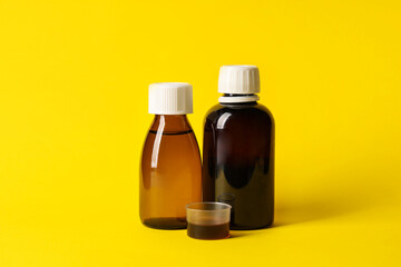 Bottles and measuring cup of cough syrup on yellow background