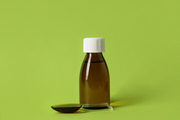 Bottle and measuring spoon of cough syrup on green background