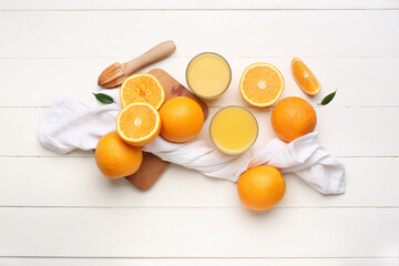 Glasses of tasty juice with fresh oranges and juicer on white wooden background