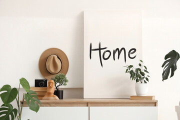 Poster with plants, books and photo camera on commode near light wall