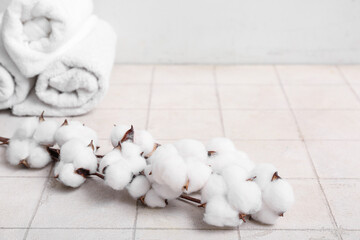 Beautiful cotton branch and clean towels on light tile table