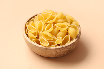 Bowl with raw pasta shells on beige background, closeup