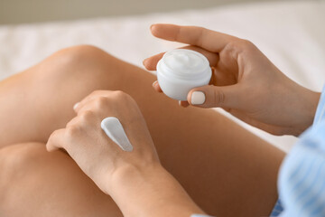 Young woman applying cream onto her hand in bedroom, closeup