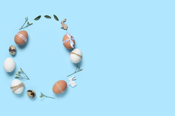 Frame made of Easter eggs, leaves, flowers and decorative bunnies on blue background