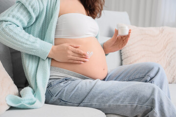 Young pregnant woman applying body cream at home