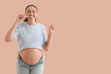 Pregnant woman brushing teeth and pointing at something on beige background