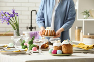 Woman holding Easter cake near table setting for Easter celebration in kitchen. Closeup
