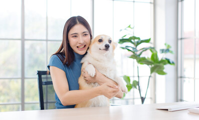 Asian young beautiful woman happy smile sitting hugging her beloved cute welsh corgi dog on chair working using computer in living room at home Love pet animals leisurely best friend lifestyle balance
