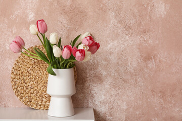 Vase with beautiful tulip flowers on table near grunge coral wall, closeup