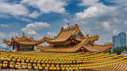 Obraz premium Chinese temple. Bright tiled roofs with curved eaves against the sky and clouds.There are red lanterns along the edges.There are figures of mythical creatures on the roof ridge.Rows of yellow lanterns