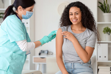 Fototapeta premium Female doctor vaccinating African-American woman in clinic