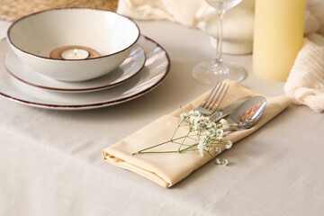 Elegant table setting with burning candle, clean plates and beautiful flowers in restaurant