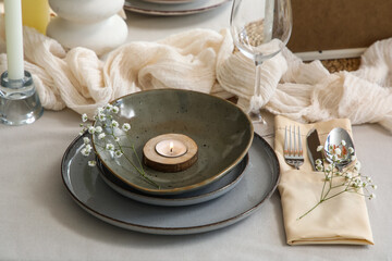 Clean plate with burning candle and beautiful flowers on served table in restaurant, closeup
