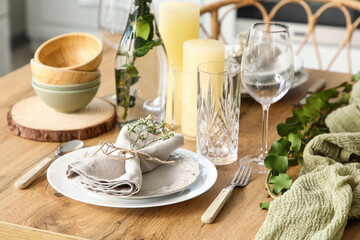 Elegant table setting with beautiful flowers and eucalyptus branches in light kitchen, closeup