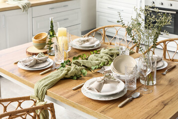 Elegant table setting with beautiful flowers, eucalyptus branches and candles in light kitchen, closeup