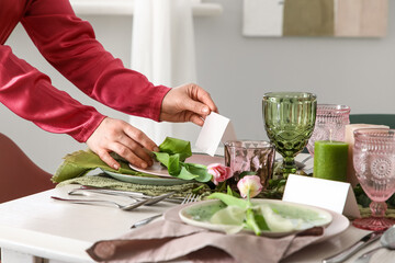 Young woman putting invitational card on elegantly served table in light dining room, closeup