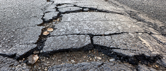 A close-up view of cracked asphalt, showing structural damage and wear, highlighting the need for road maintenance.
