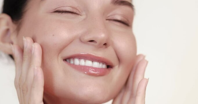 Caucasian woman smiles with eyes closed while massaging her glowing skin in slow motion. Perfect for skincare, facial massage, cosmetics, or beauty routine promo content.