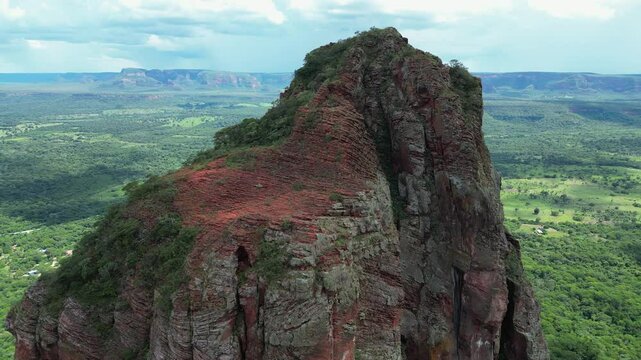 Aerial orbits rugged summit of sandstone pillar above green forest