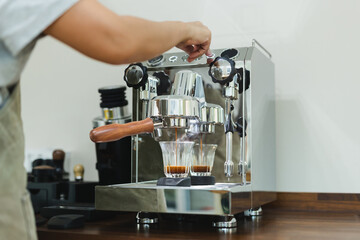 Hands of female barista pressing button on machine while making fresh coffee..