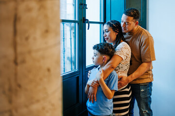 Pregnant mother, father and son looking thoughtfully out the window, embracing each other