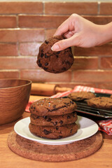 Dipping a tasty chocolate chip handmade cookie into a glass of milk at a wooden table, closeup. Selective focus