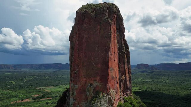 Aerial ascends red sandstone pillar in lush green valley, dark clouds