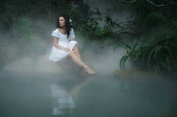 Fototapeta premium A princess or fairy in a mystical garden by the lake surrounded by trees and fog. Fairyland