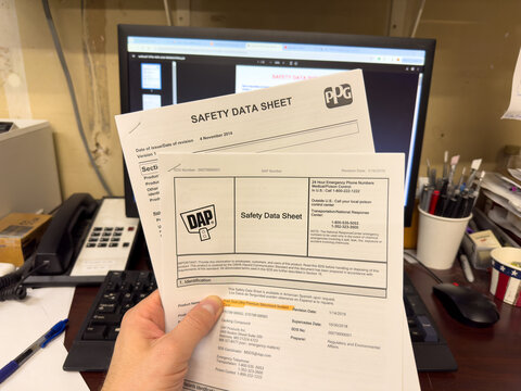 Holding printed SDS, safety data sheets in front of computer.
