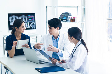 Fototapeta premium Medical Team Discussing Patient Data with Digital Devices.A group of medical professionals including doctors and a nurse are having a meeting in a bright office. They are reviewing patient information