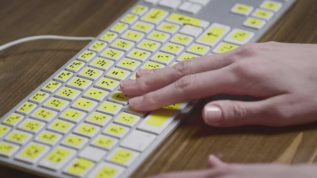 Close-up of a computer keyboard with braille. A blind girl is typing words on the buttons with her hands. Technological device for visually impaired people. Tactilely touches bumps on the keys
