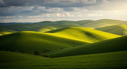 Obraz premium Sunlit Green Rolling Hills Under a Cloudy Sky